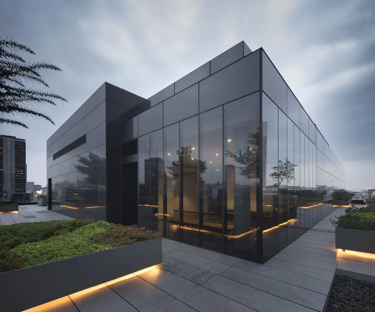 Dark glass building with lit planters at dusk